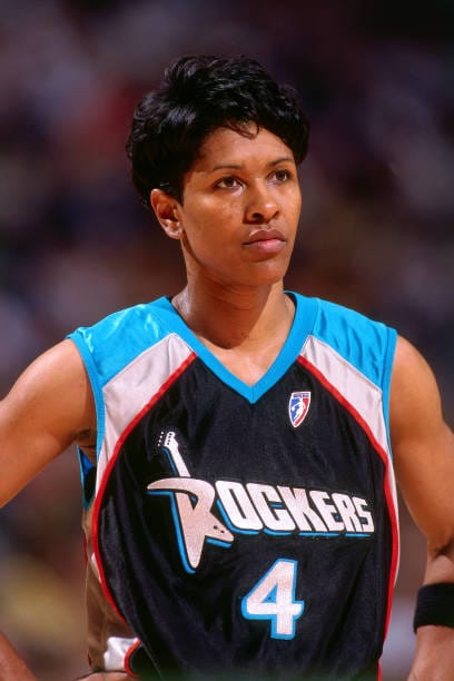 Basketball player Lynette Woodard standing during a game in 1997, wearing a black jersey with blue and silver shoulders on the jersey. 